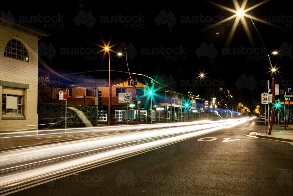 Light trails from cars going through a green traffic light at night - Australian Stock Image