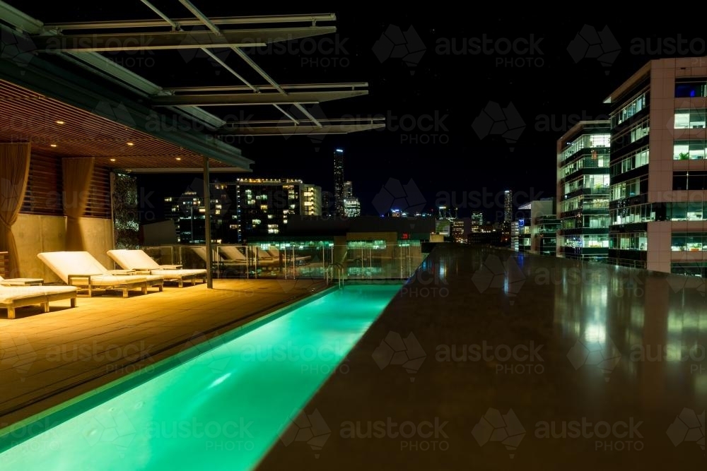 Lighted rooftop swimming pool at night, overlooking the city - Australian Stock Image