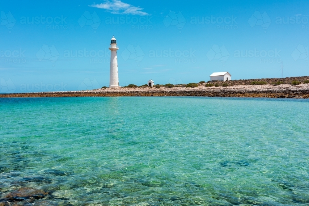 Lighthouse and out buildings on stony land near shallow water - Australian Stock Image