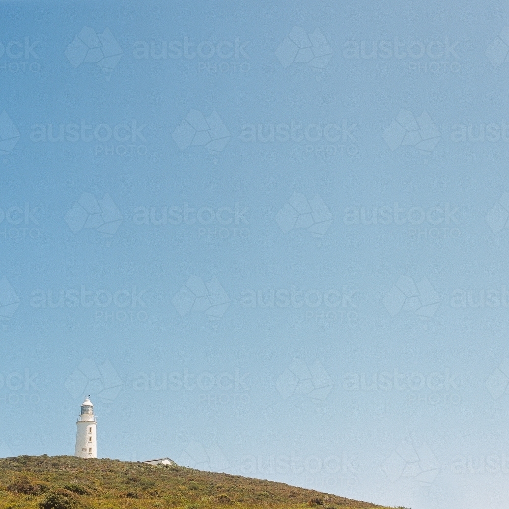 Lighthouse in the distance on a headland with blue sky background - Australian Stock Image