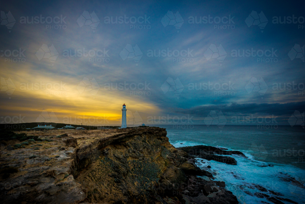 Lighthouse stands tall on a rugged headland at dusk - Australian Stock Image