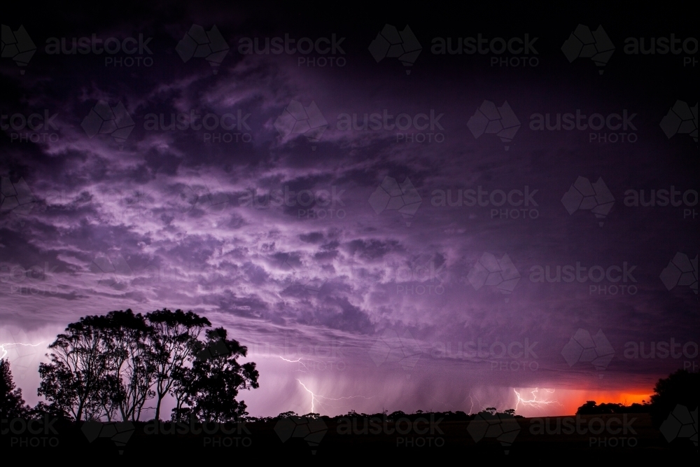 Lightning strikes in purple sky at sunset - Australian Stock Image