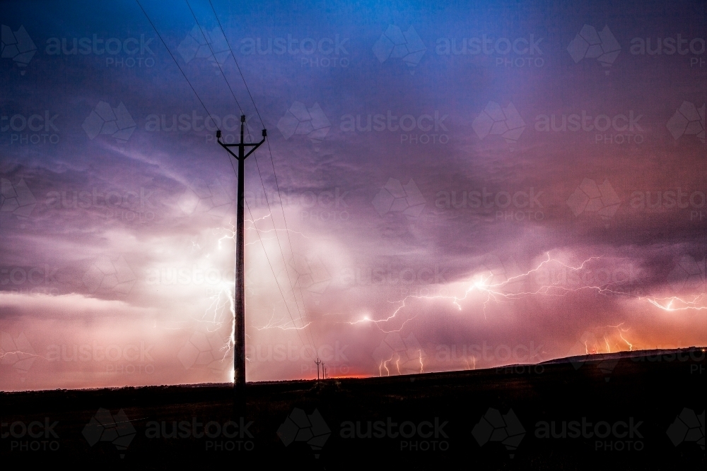 Lightning striking at sunset behind power poles - Australian Stock Image