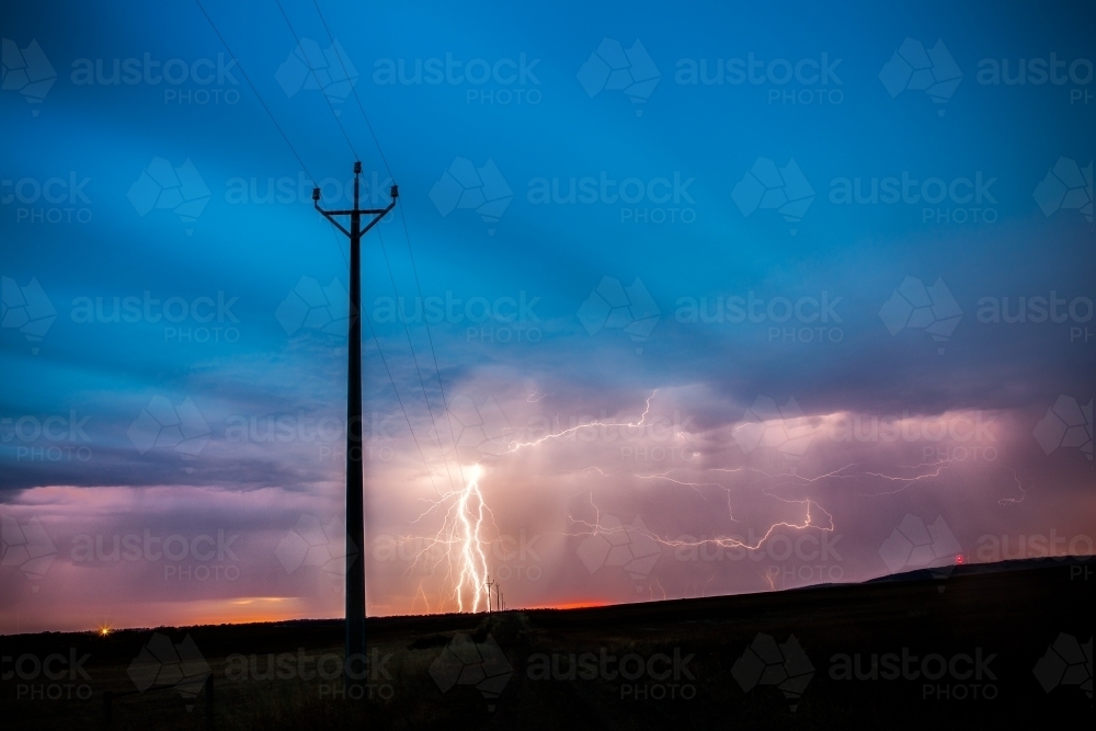 Lightning striking in ominous sky behind power pole - Australian Stock Image