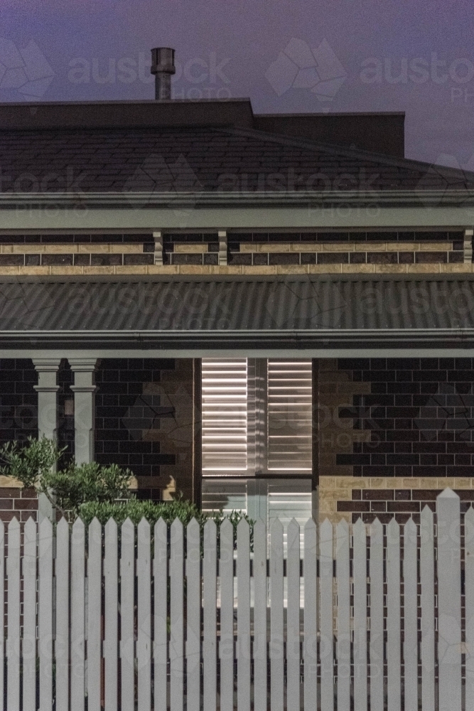 lights on in an inner city heritage home with picket fence at dusk - Australian Stock Image