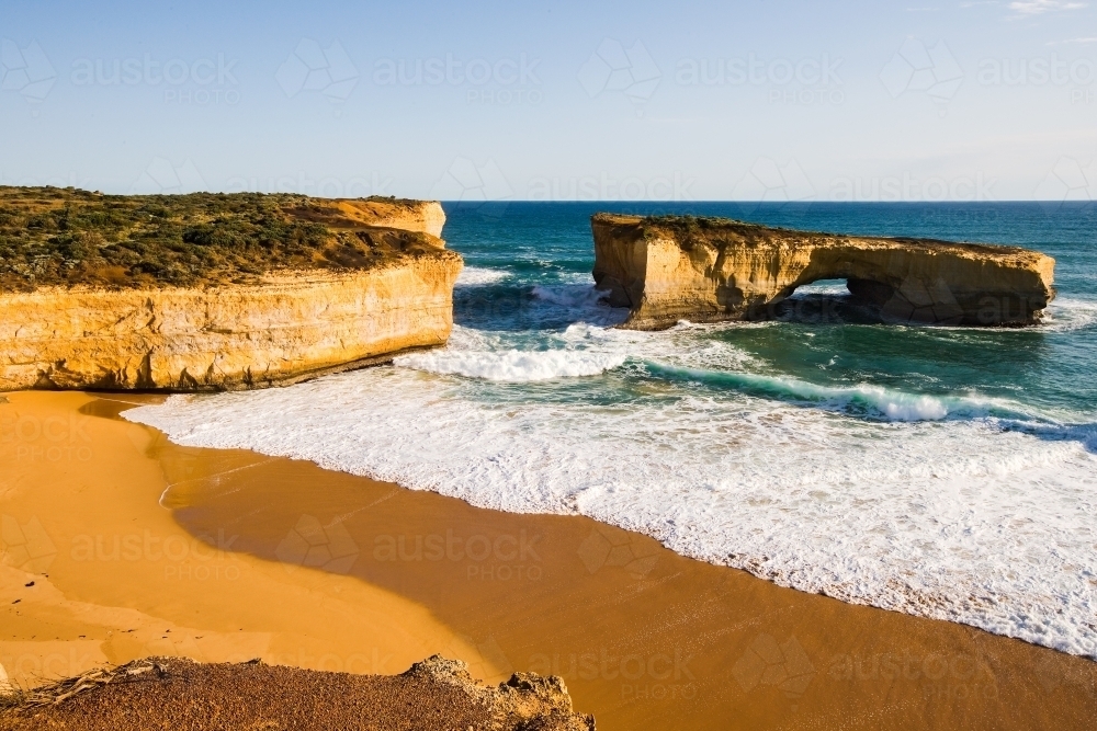 Limestone stack with waves crashing on beach - Australian Stock Image