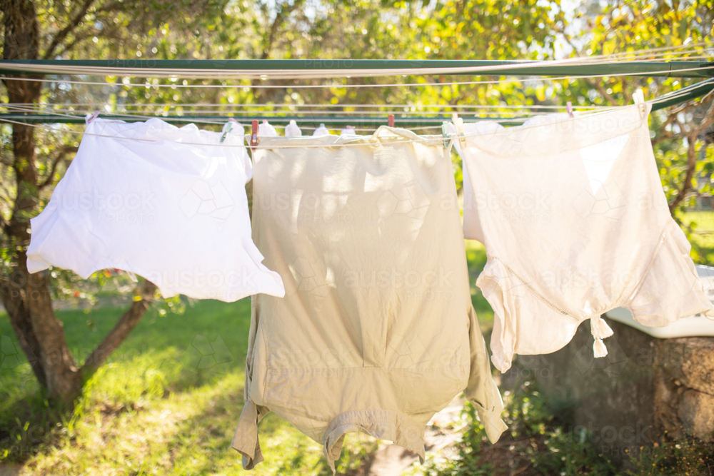 Linen shirts hanging on washing line in dappled sunlight on sunny day - Australian Stock Image