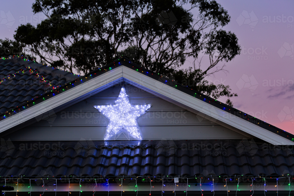 Lit up star christmas lights on house at dusk with silhouetted gum tree behind - Australian Stock Image