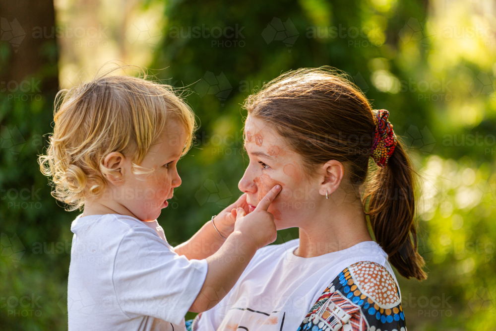 Little aboriginal boy touching ochre face paint on big sister - Australian Stock Image