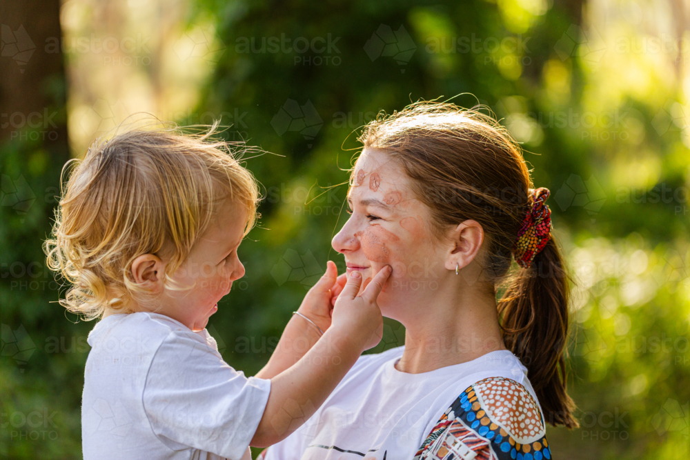 Little aboriginal boy touching ochre face paint on big sister - Australian Stock Image