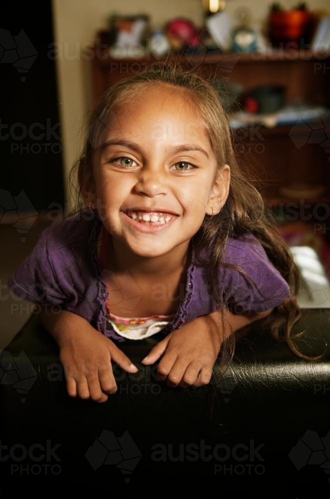 Little Aboriginal Girl on Back of Couch Smiling - Australian Stock Image