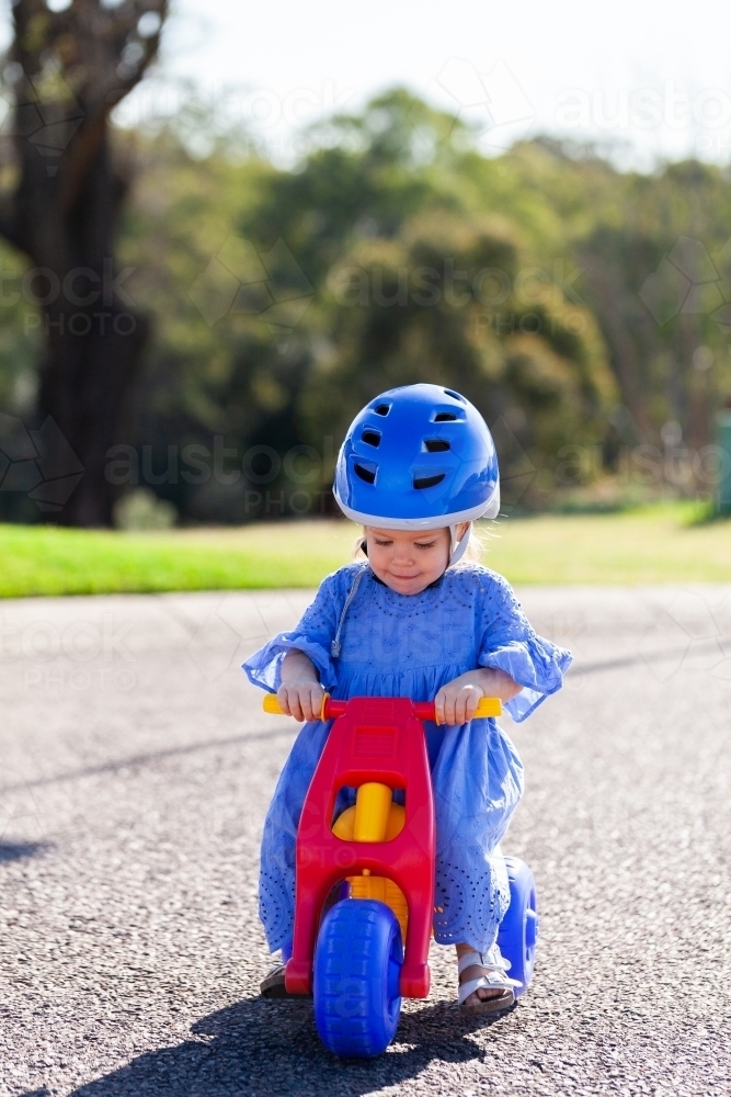 Little Aussie girl in blue dress and helmet riding trike down road - Australian Stock Image