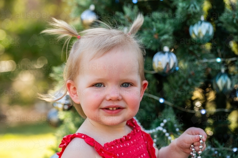 Little Aussie girl in red dress by Christmas tree - Australian Stock Image