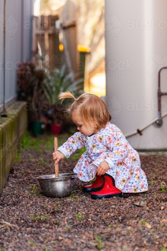 Little Aussie kid in alleyway beside house mixing in bowl with stick - Australian Stock Image