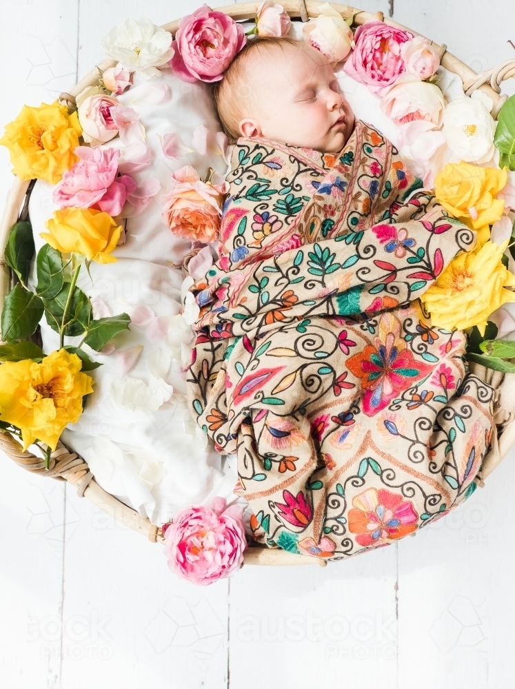 Little baby girl asleep in a basket of flowers. - Australian Stock Image