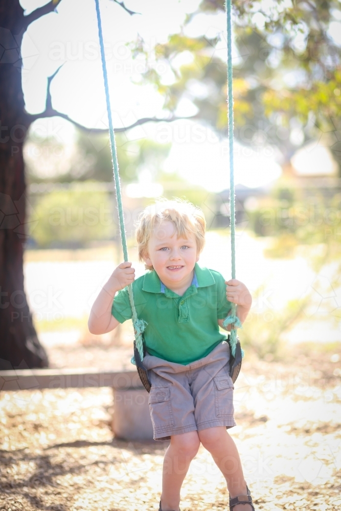 Little blond boy playing on swing at kindergarten - Australian Stock Image