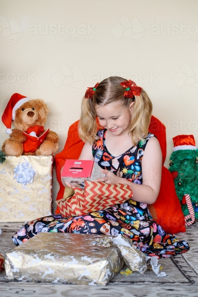 Little blonde girl excitedly looking at a Christmas gift she has just unwrapped - Australian Stock Image