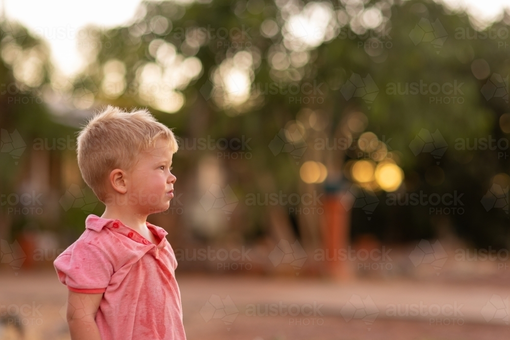 little blonde-haired boy with dishevelled shirt offset with blurry background - Australian Stock Image
