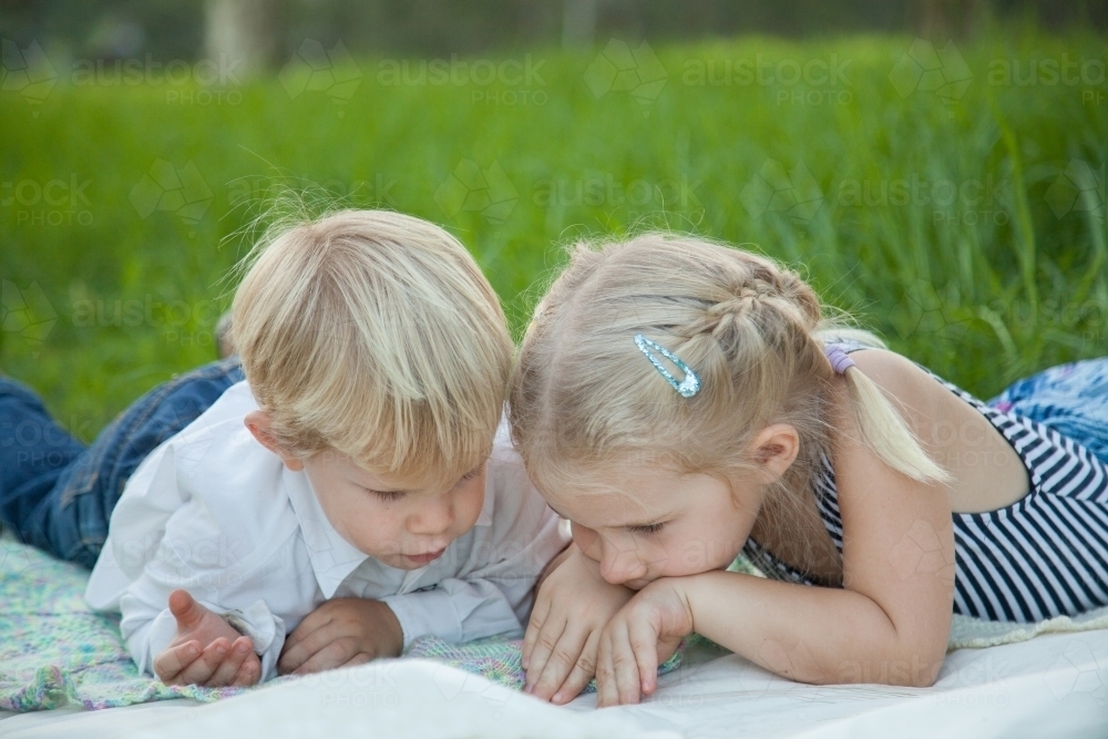 Little boy and girl watching a bug crawling on a mat - Australian Stock Image