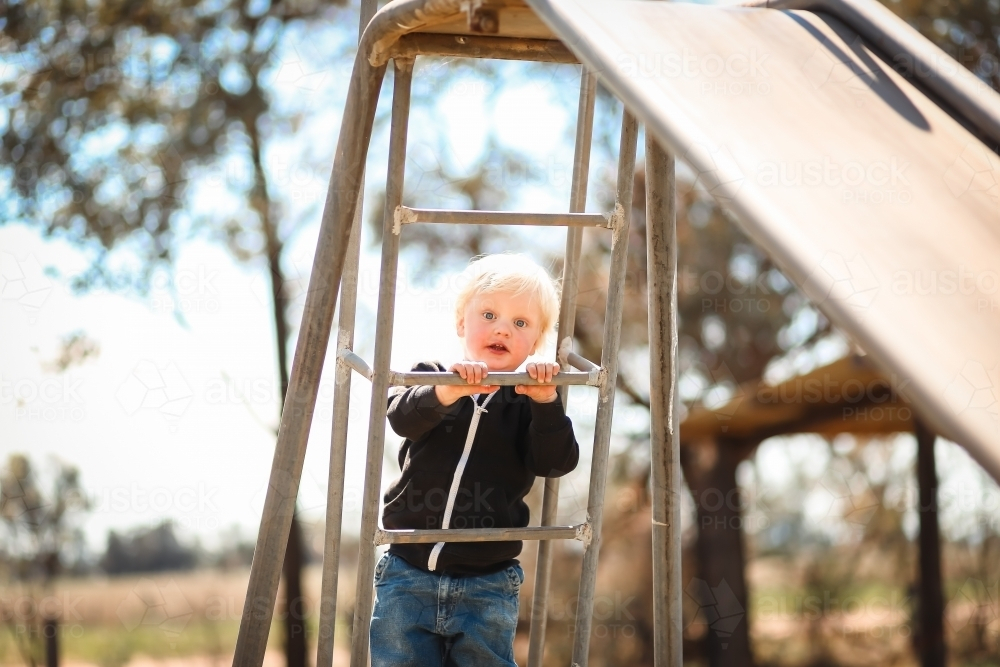 Little boy climbing old-fashioned metal slide in regional playground - Australian Stock Image