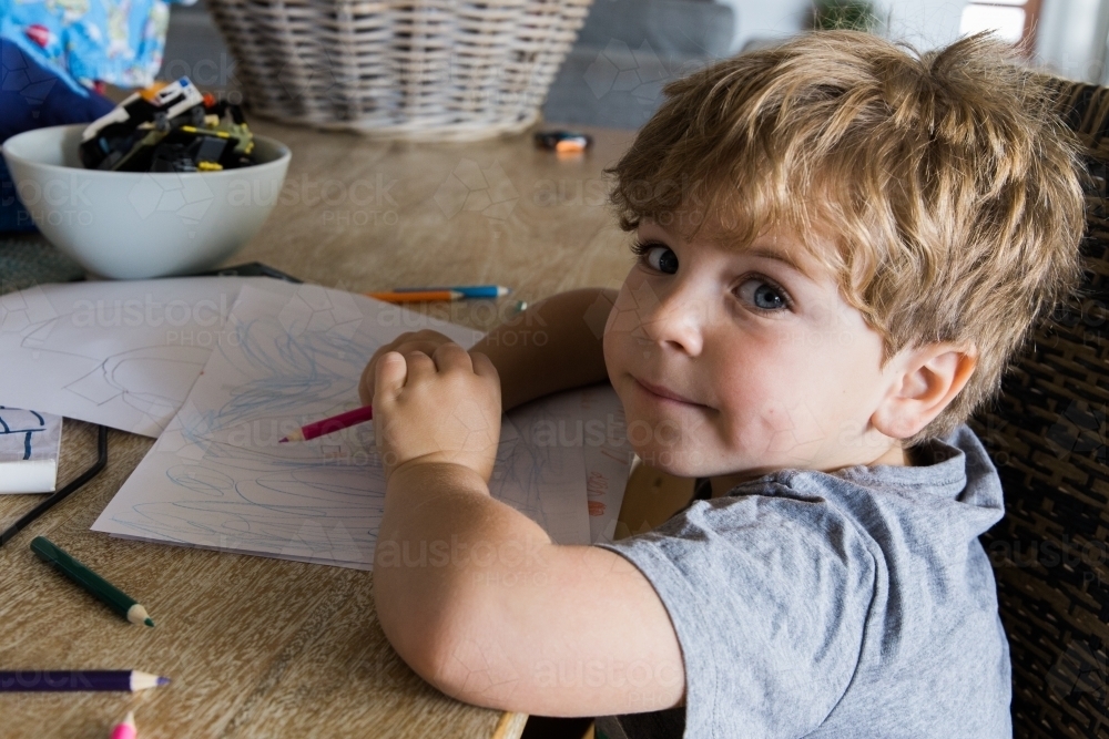 Little boy drawing with pencils at a table - Australian Stock Image