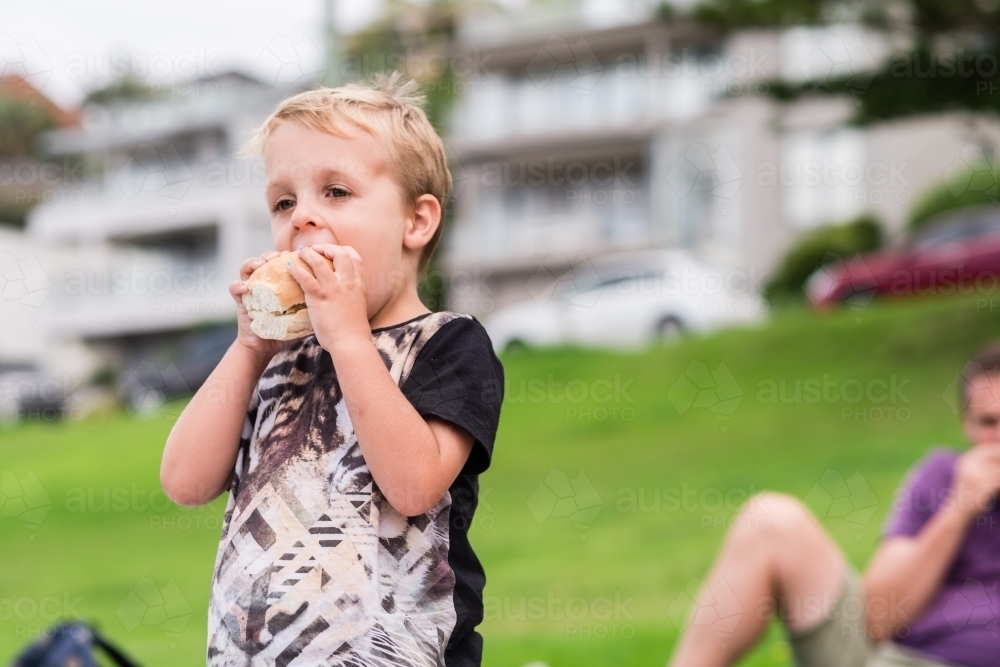 little boy eating breadroll at a picnic - Australian Stock Image