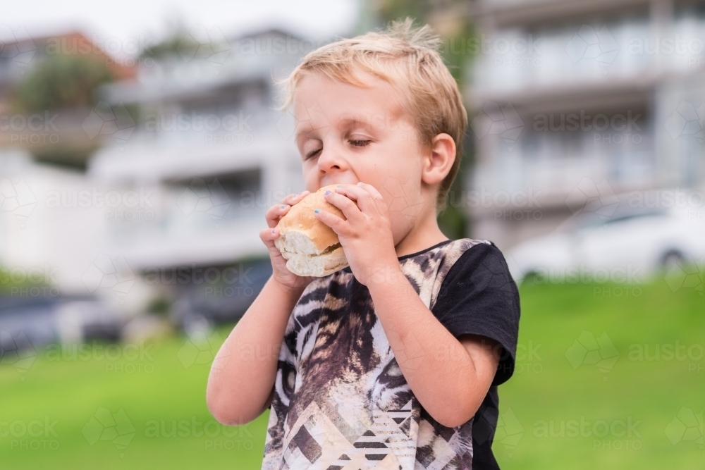 little boy eating breadroll at a picnic - Australian Stock Image