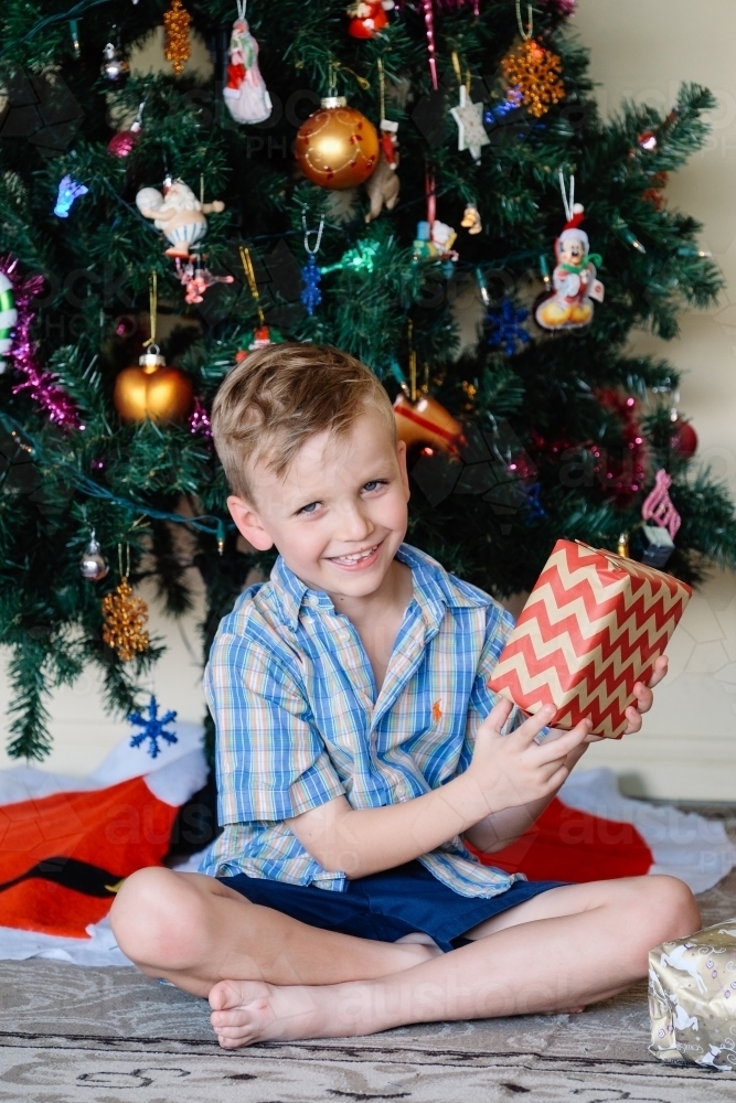 Little boy happily holding a present on Christmas day - Australian Stock Image