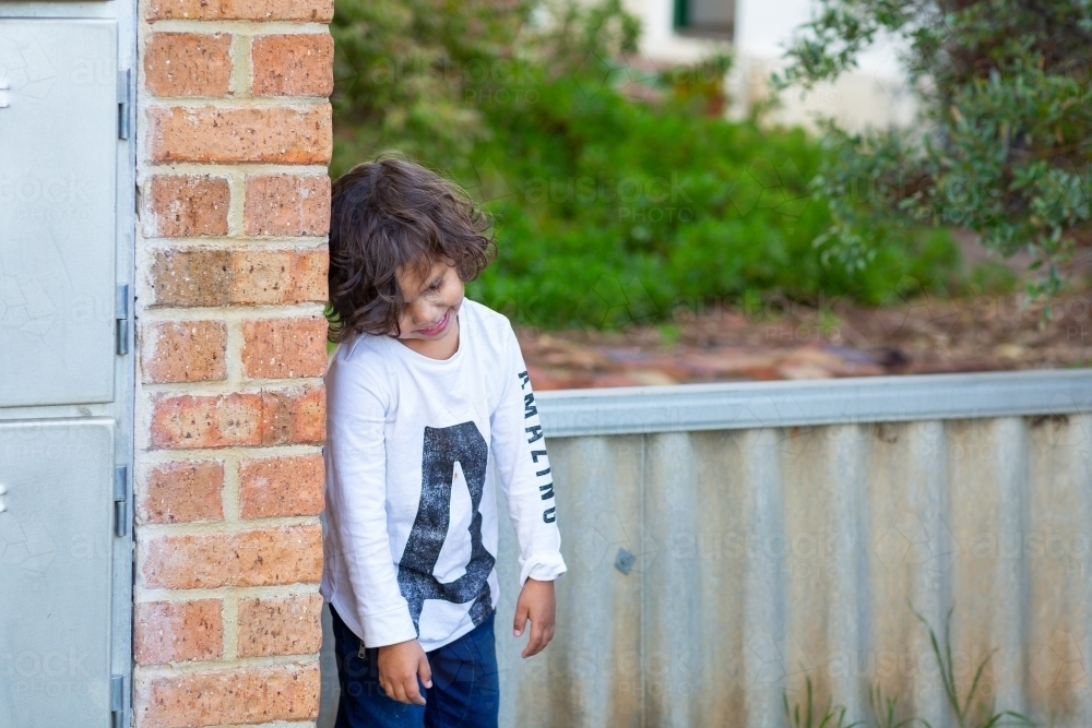 Little boy hiding behind brick wall - Australian Stock Image