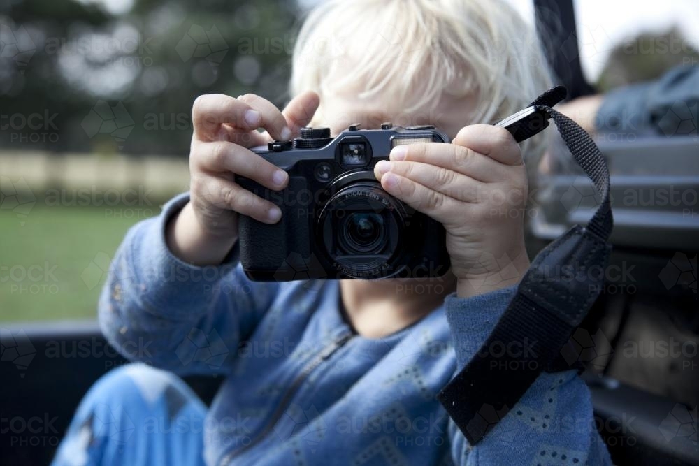 Little boy holding up digital camera to take a photo - Australian Stock Image