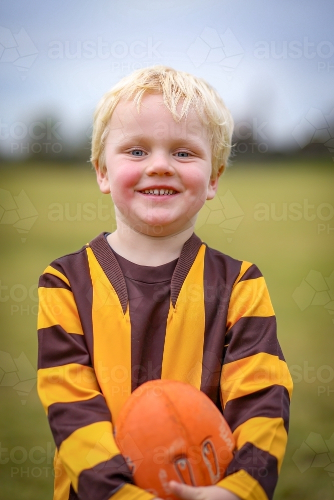 Little boy in Aussie Rules Football uniform on field with ball - Australian Stock Image
