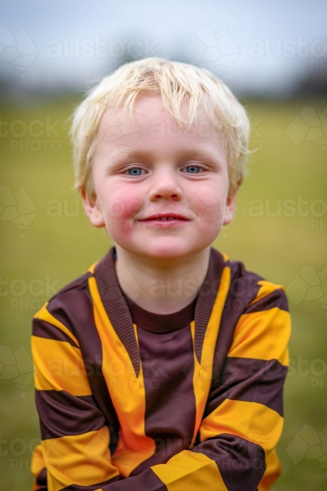 Little boy in Aussie Rules Football uniform on field with ball - Australian Stock Image