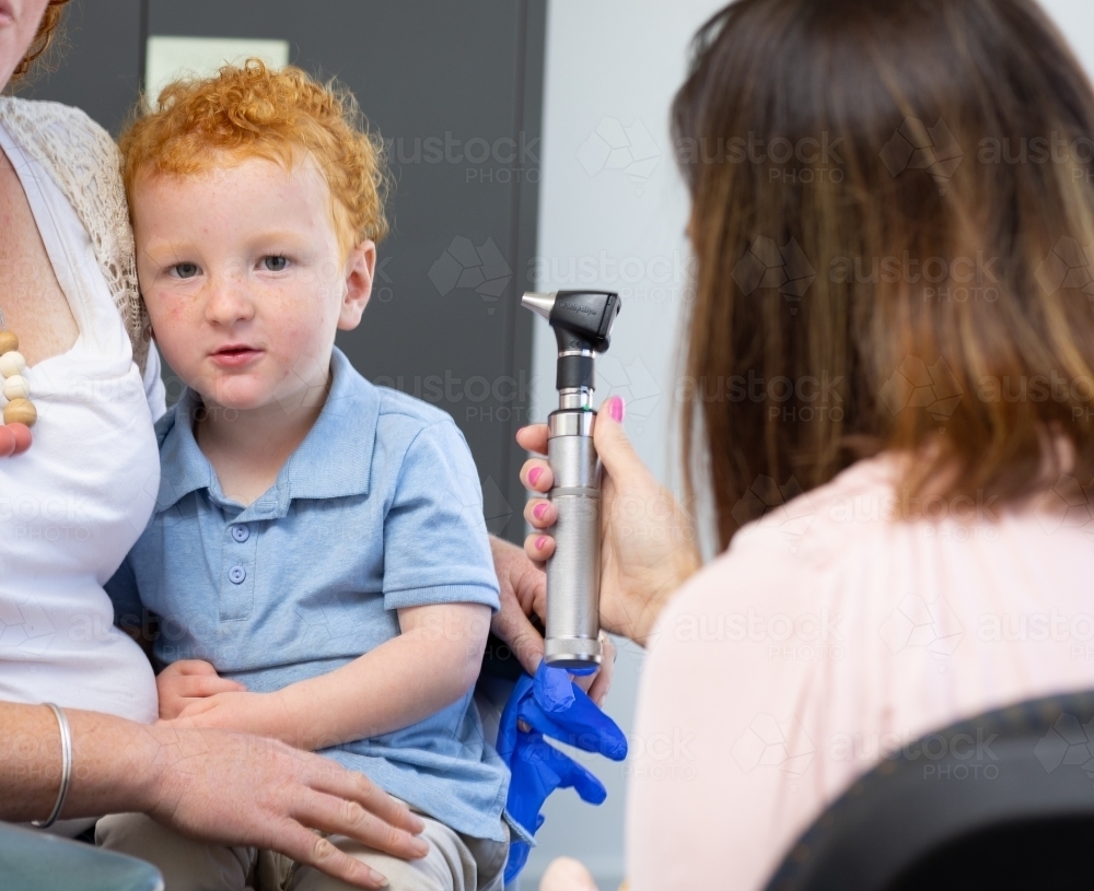 little boy looking at camera as nurse holds otoscope - Australian Stock Image