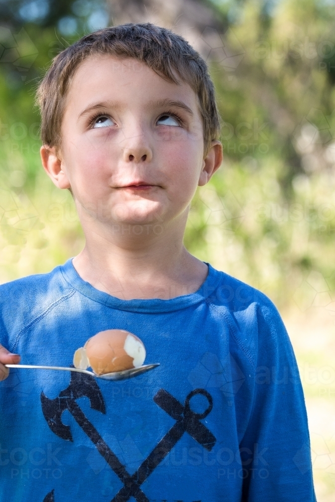 Little boy makes funny face with egg and spoon - Australian Stock Image