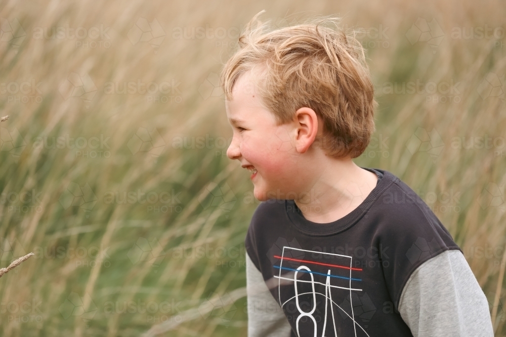 Little boy on nature walk smiling in long grass - Australian Stock Image