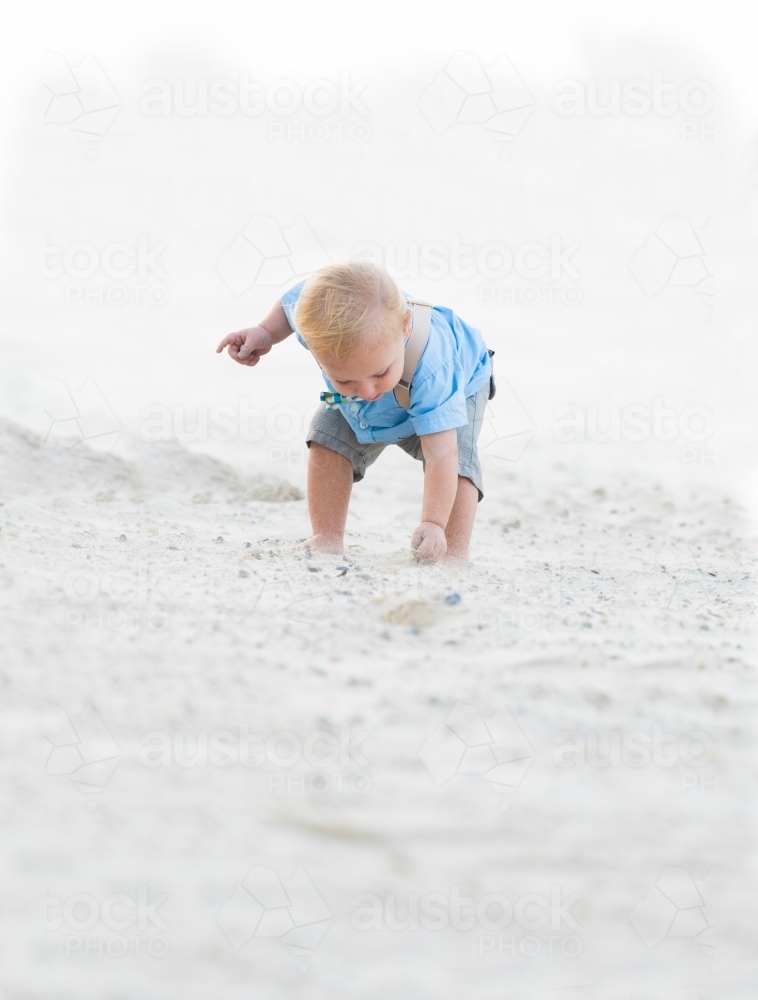 Little boy picking up a shell on the beach - Australian Stock Image