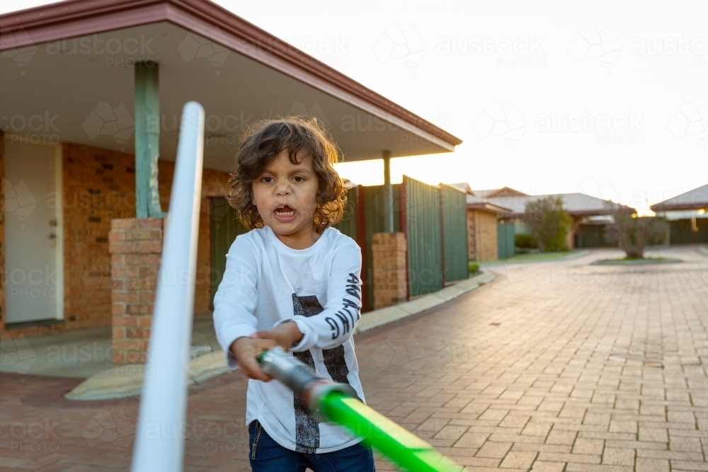 Little boy play fighting with toy lightsaber - Australian Stock Image