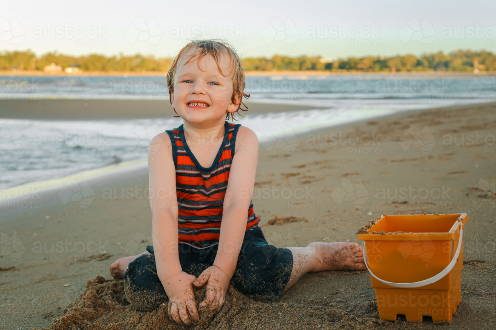 Little boy playing with diggers and bucket on the sand at the beach - Australian Stock Image