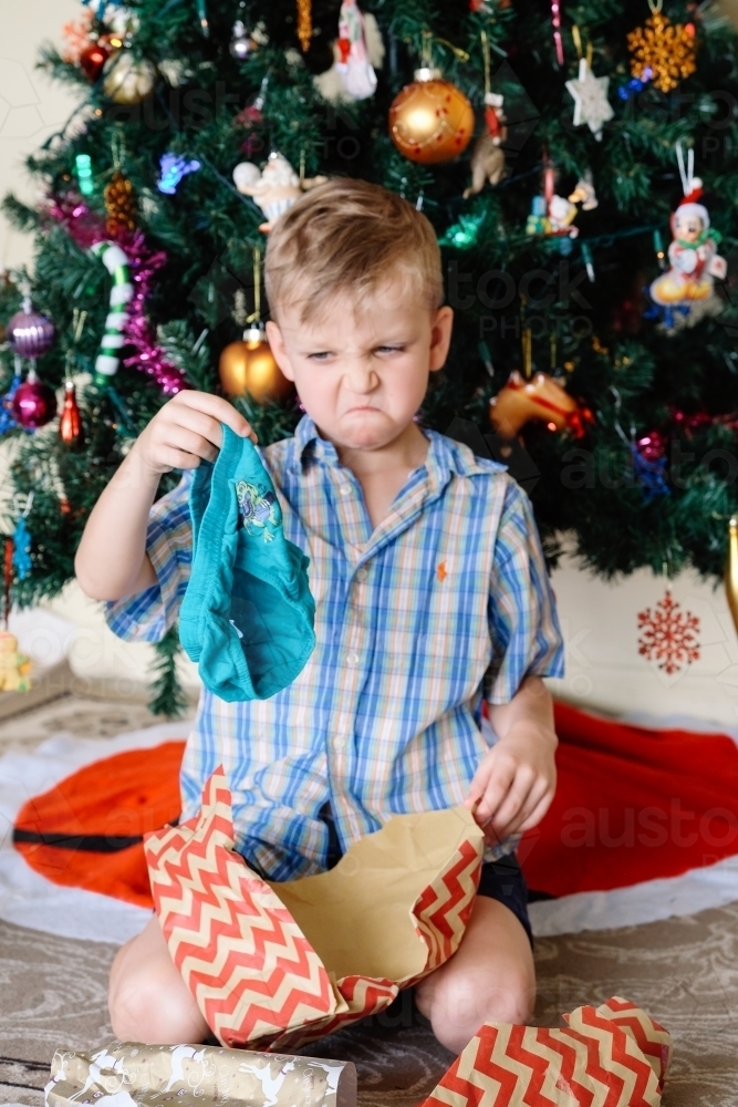 Little boy pulling a face, unhappy with a gift of underpants he has received on Christmas day - Australian Stock Image