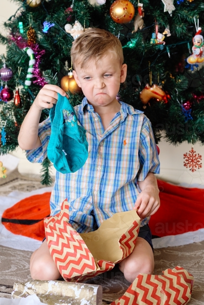 Little boy pulling a sad face, unhappy with a gift of underpants he has received on Christmas day - Australian Stock Image