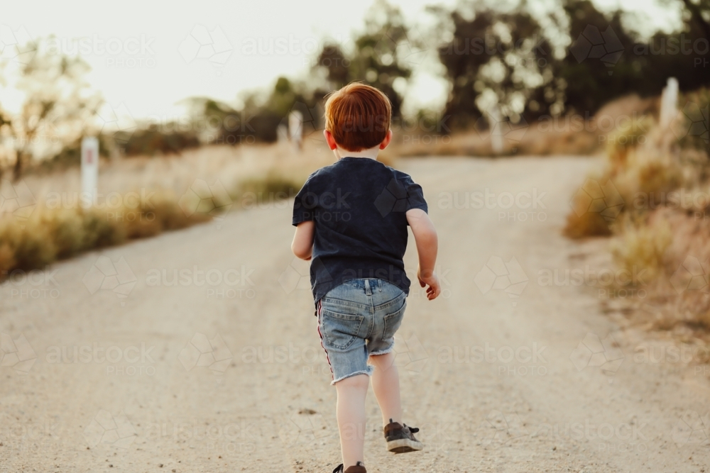 Little boy running along rural gravel road - Australian Stock Image