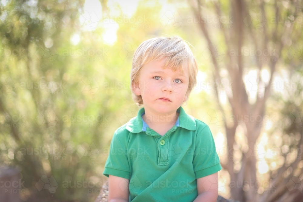 Little boy sitting in kindergarten yard with serious expression - Australian Stock Image