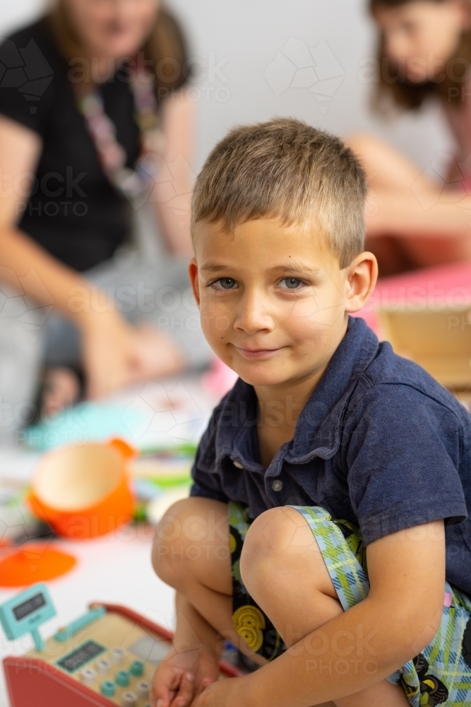 little boy squatting down with blurred people in background - Australian Stock Image