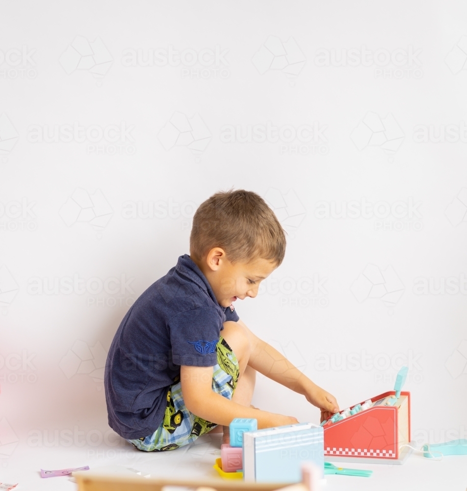 little boy squatting playing with toys against white background - Australian Stock Image