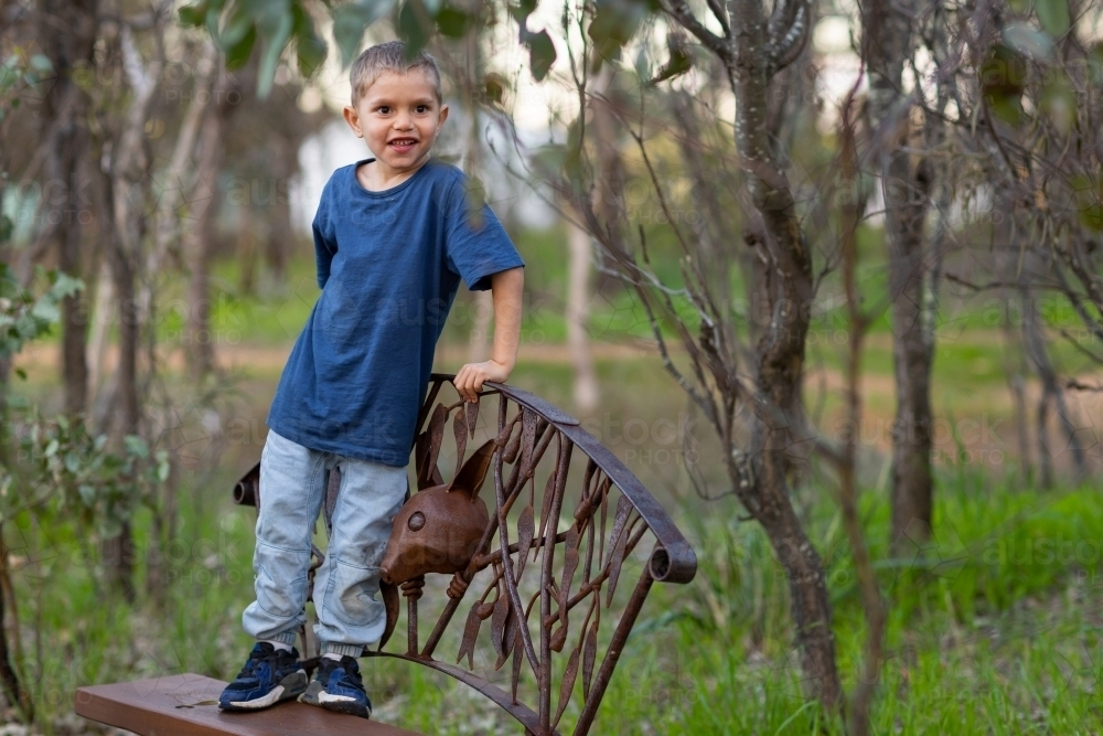 little boy standing on park bench with trees in background - Australian Stock Image