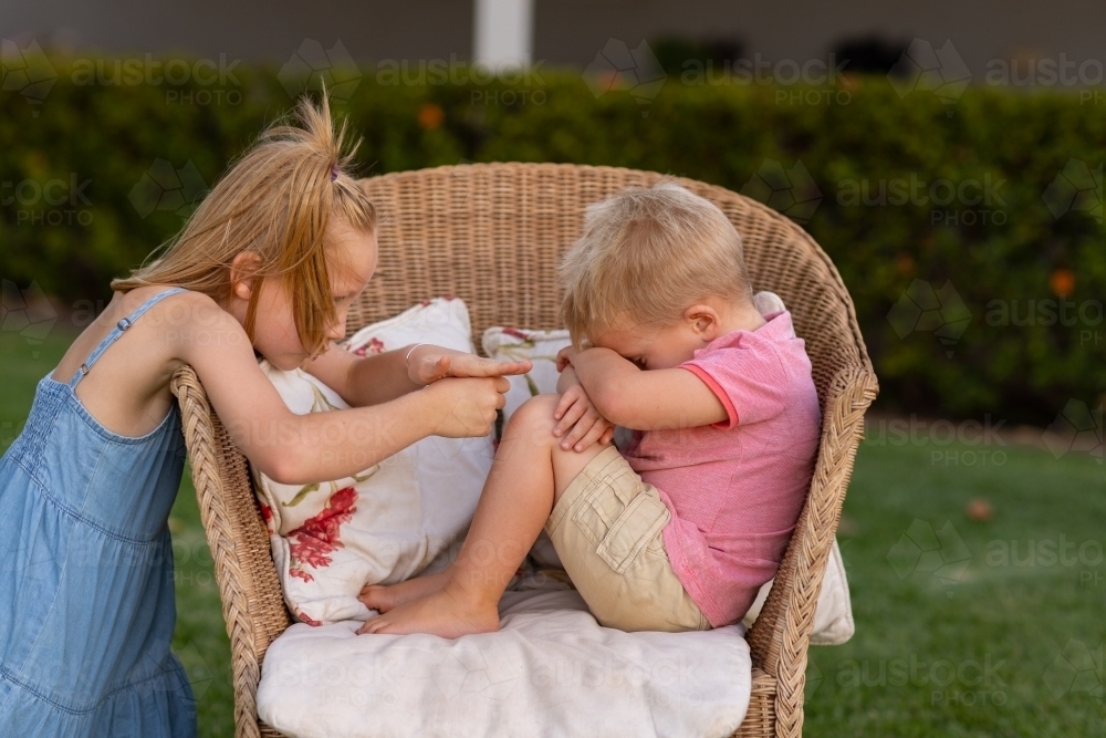little boy sulking with big sister trying to cheer him up - Australian Stock Image