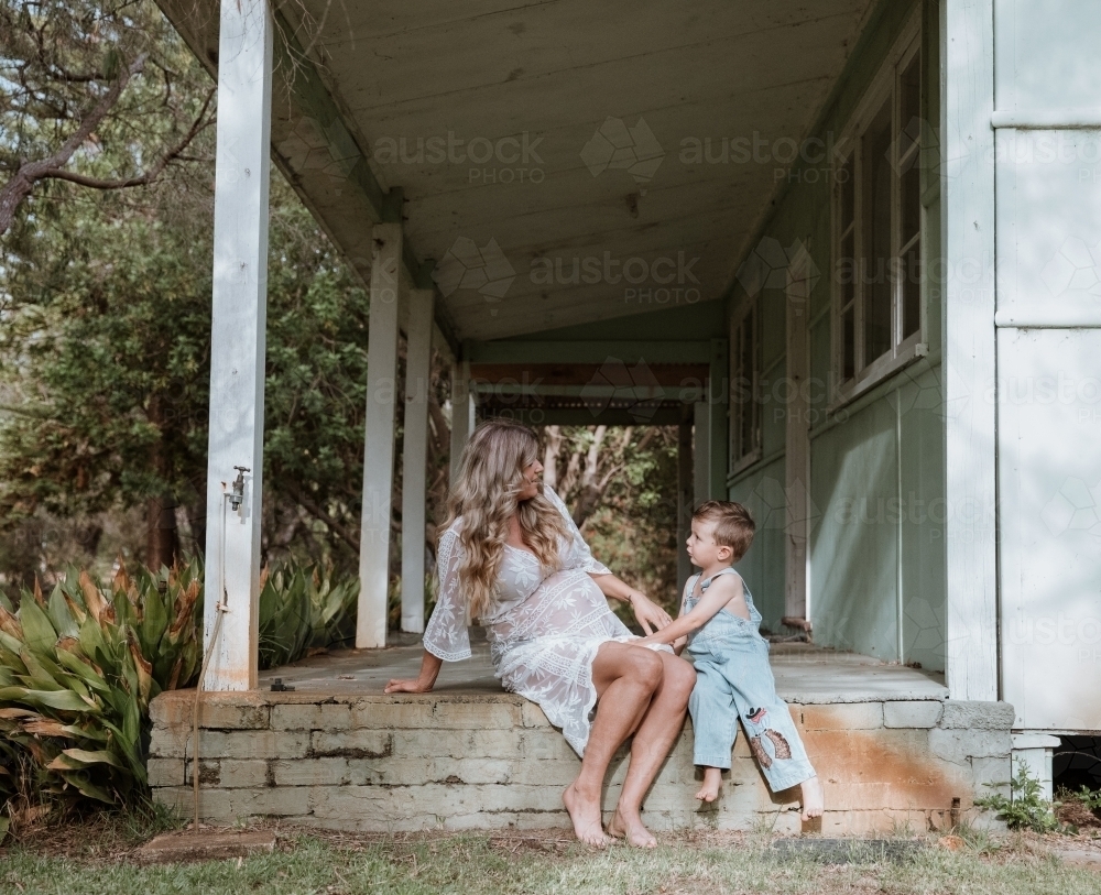 Little boy talking with his mother on the steps of front verandah - Australian Stock Image