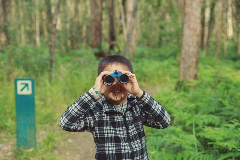 Little boy using binoculars in the forest - Australian Stock Image