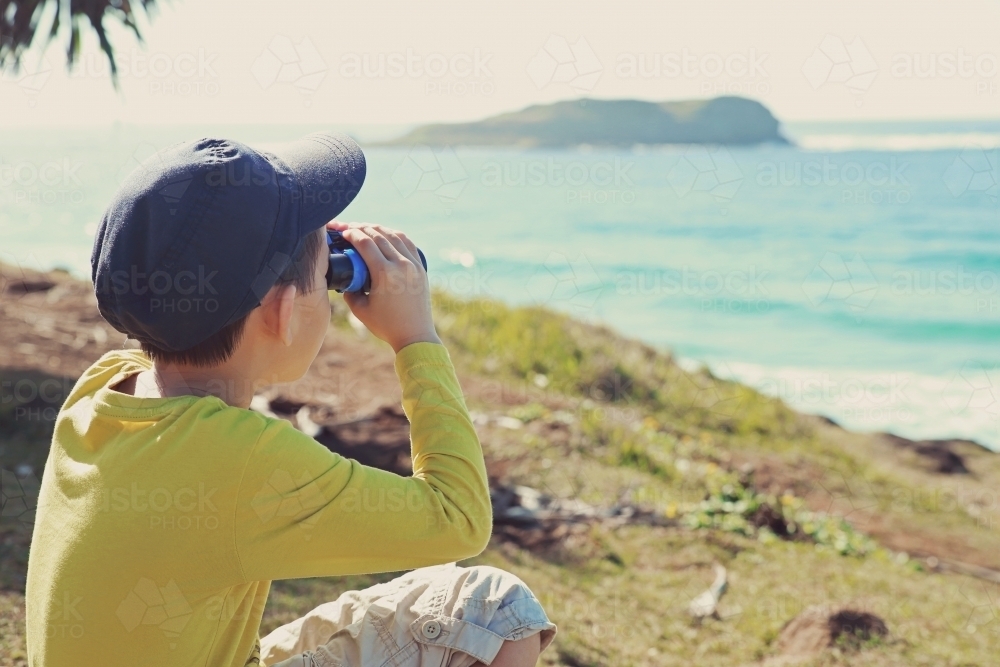 Little boy using binoculars looking over oceans - Australian Stock Image