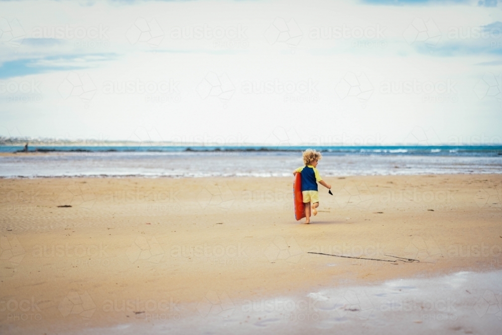 Little boy walking toward the water at the beach - Australian Stock Image